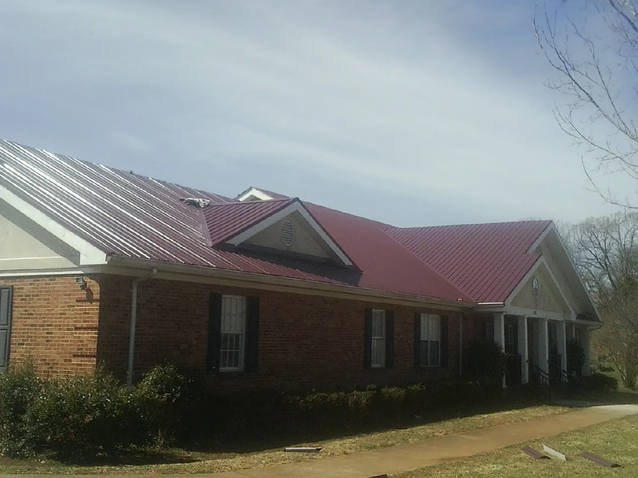 Red metal roof with gabled entries on a long brick building, from a Hail Damage Roof Repair job in Pottstown