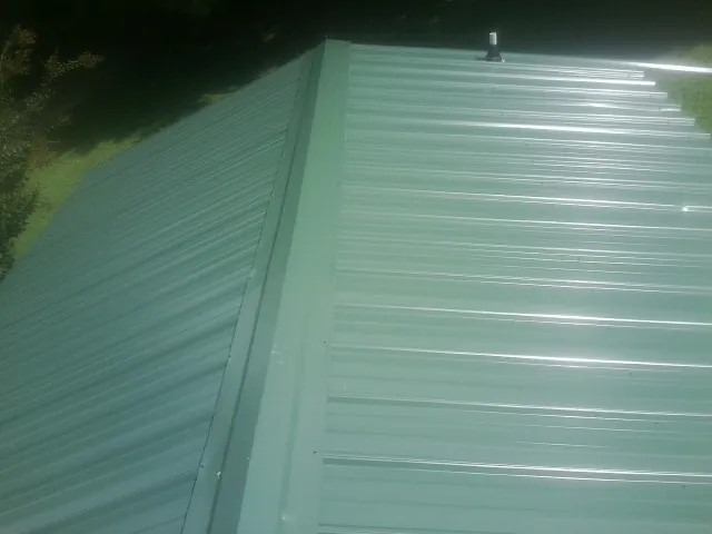 New green metal panels meeting at the ridge of a roof — Flat Roof Repair work by our crew in Pottstown