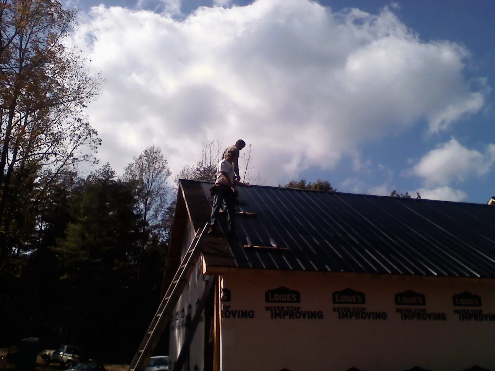Roofer fastening dark metal panels high against a cloudy sky, from a Roof Inspection job in Pottstown