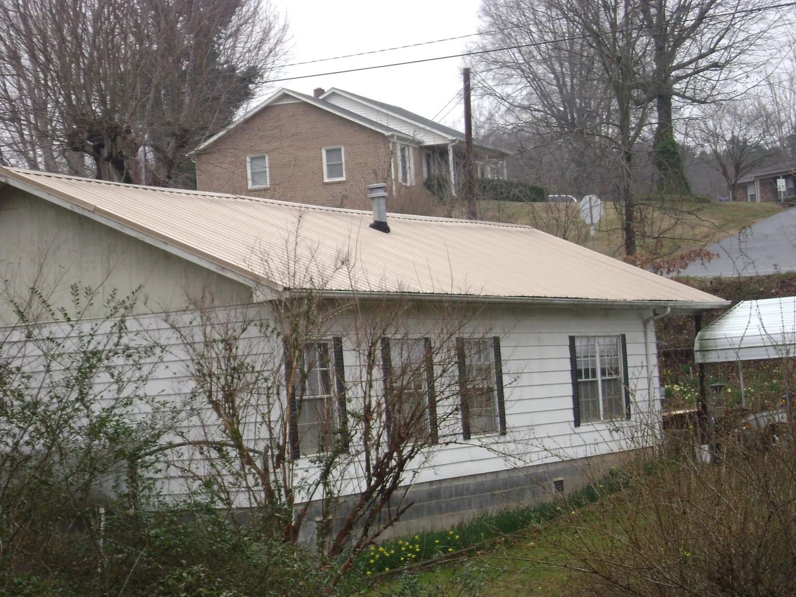 Tan metal roof on a white sided house set into a hillside — Commercial Roofing by Roofing Brothers in Pottstown